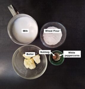 Ingredients for béchamel sauce: milk, flour, butter, freshly grated nutmeg, and white peppercorns arranged together.